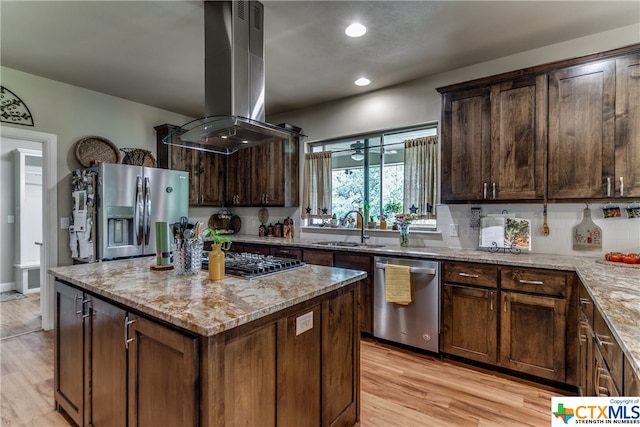 kitchen with light stone countertops, light wood-type flooring, stainless steel appliances, island range hood, and sink