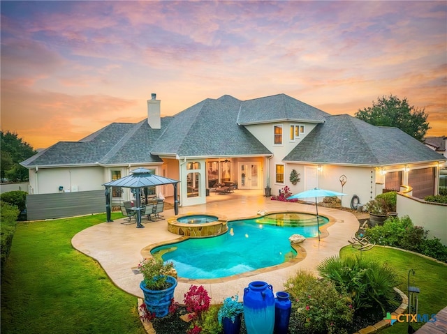 pool at dusk with an in ground hot tub, a gazebo, a lawn, and a patio