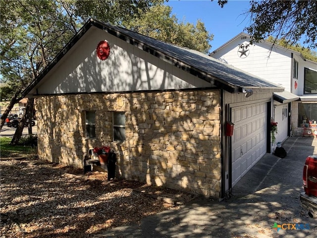 view of side of home with an attached garage, stone siding, and roof with shingles