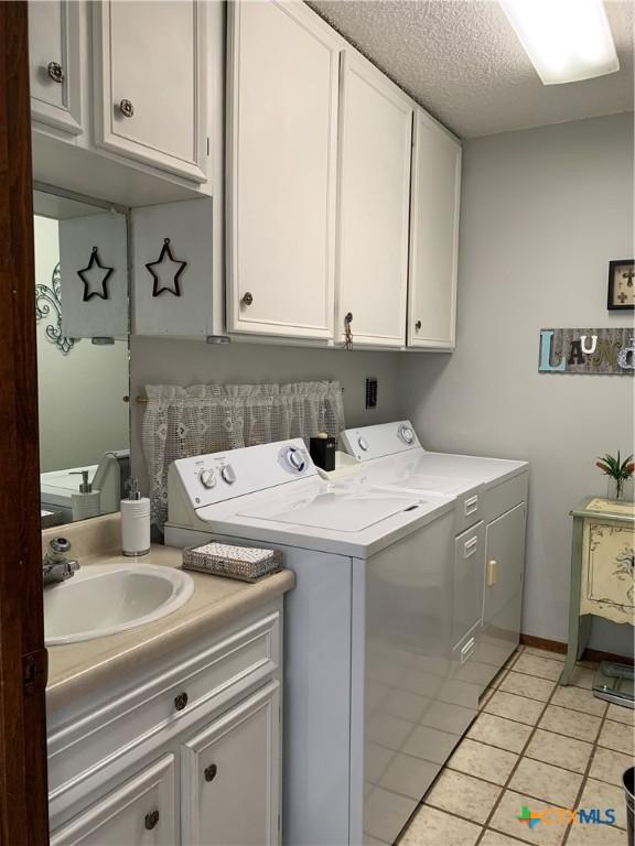 laundry room with a textured ceiling, light tile patterned flooring, a sink, independent washer and dryer, and cabinet space