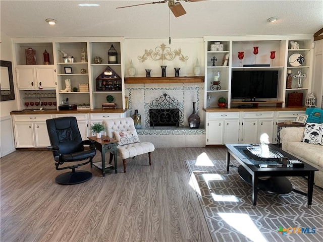 living room featuring ceiling fan, light wood-type flooring, and a tile fireplace