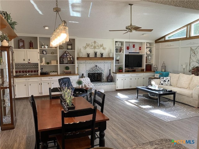 dining area featuring built in shelves, light wood finished floors, vaulted ceiling, a textured ceiling, and ceiling fan