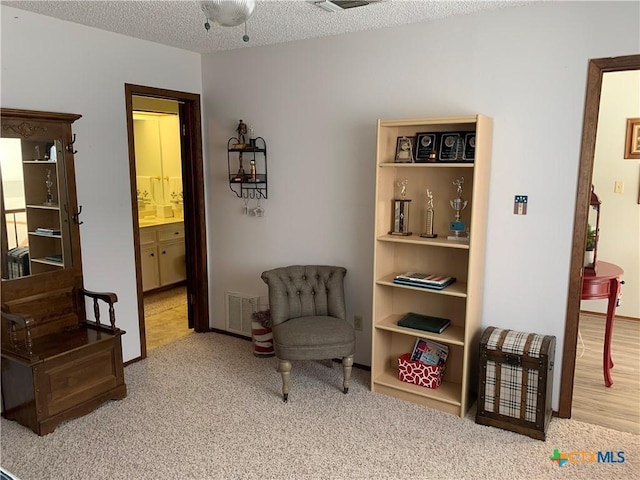 sitting room with visible vents, a textured ceiling, and carpet flooring