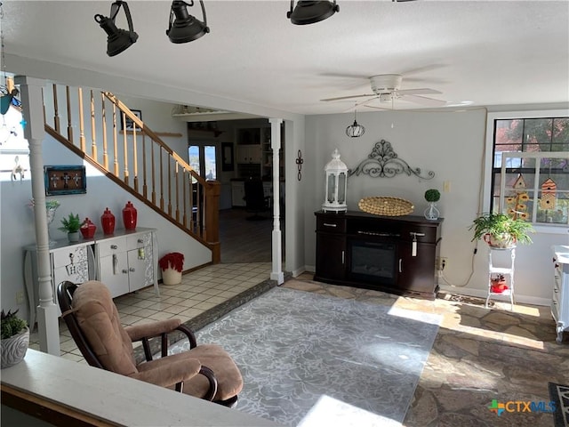 living area with ceiling fan, stairway, baseboards, and a glass covered fireplace