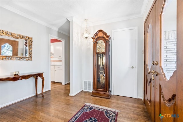 foyer with crown molding, wood finished floors, visible vents, and baseboards