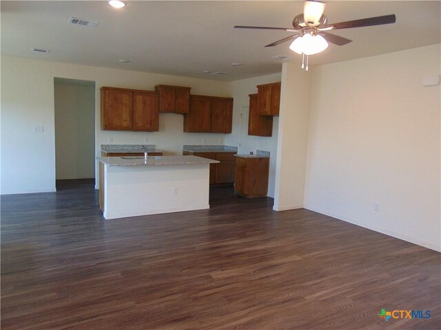 3101 Salt Fork Dr, Killeen, TX 76549 - kitchen featuring a sink, brown cabinets, dark wood-type flooring, light stone countertops, and a center island with sink