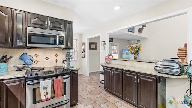 689 Abels Way, Canyon Lake, TX 78133 - kitchen featuring appliances with stainless steel finishes, decorative backsplash, dark brown cabinetry, light stone finish flooring, and light stone counters