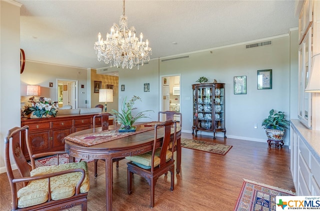 dining room with a chandelier, hardwood / wood-style floors, ornamental molding, and a textured ceiling