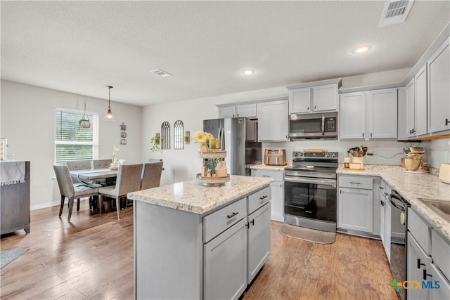 6402 Castle Gap Dr, Killeen, TX 76549 - kitchen with appliances with stainless steel finishes, a kitchen island, gray cabinetry, light wood finished floors, and light stone countertops