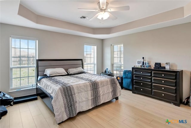 bedroom featuring visible vents, a raised ceiling, light wood-style flooring, and a ceiling fan