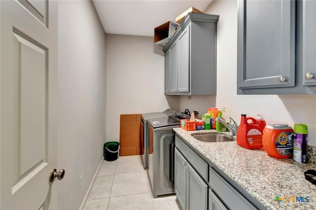 washroom featuring a sink, washing machine and dryer, cabinet space, light tile patterned floors, and baseboards