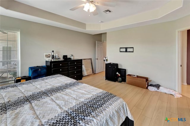 bedroom with visible vents, a ceiling fan, a tray ceiling, and wood finished floors