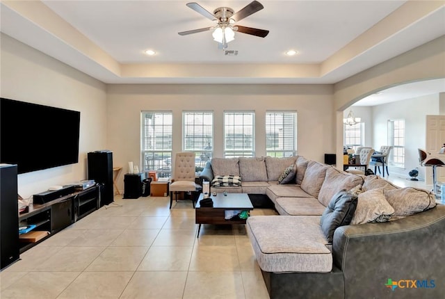 living room with a raised ceiling, light tile patterned floors, ceiling fan with notable chandelier, and arched walkways