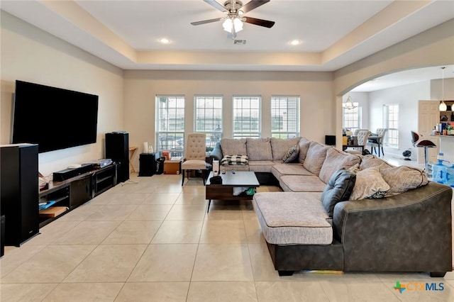 living room with a raised ceiling, light tile patterned floors, arched walkways, and ceiling fan