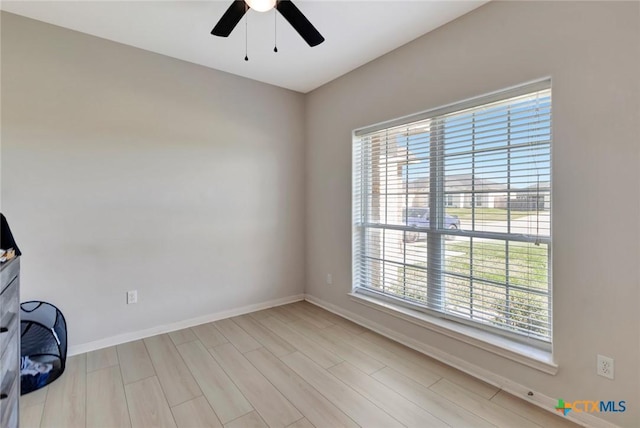 spare room featuring light wood-style flooring, a ceiling fan, and baseboards