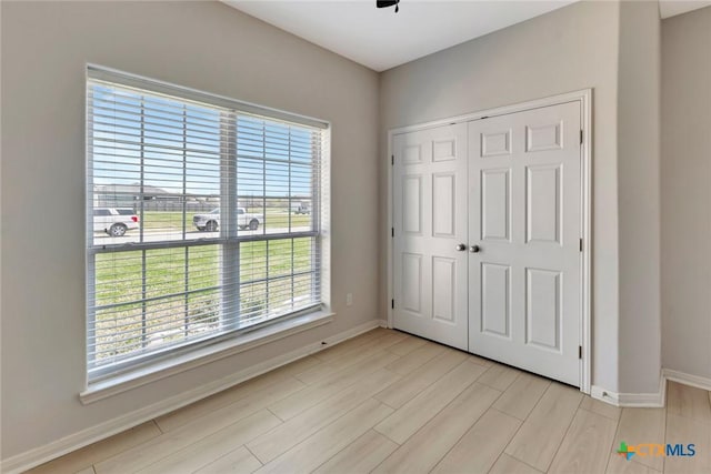 unfurnished bedroom featuring light wood-style flooring, baseboards, and a closet