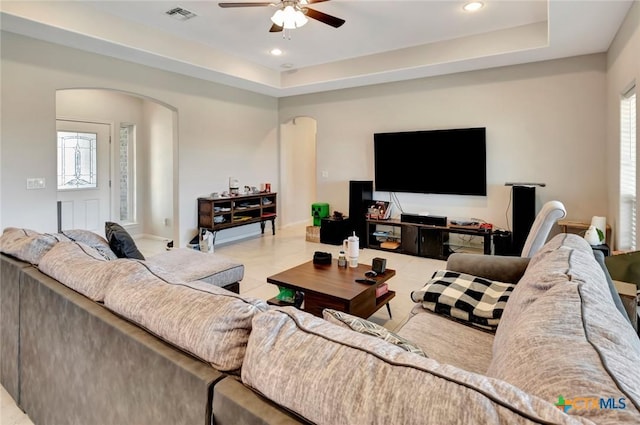 living area with a ceiling fan, a raised ceiling, visible vents, and arched walkways