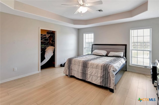 bedroom with a raised ceiling, visible vents, light wood-type flooring, and baseboards