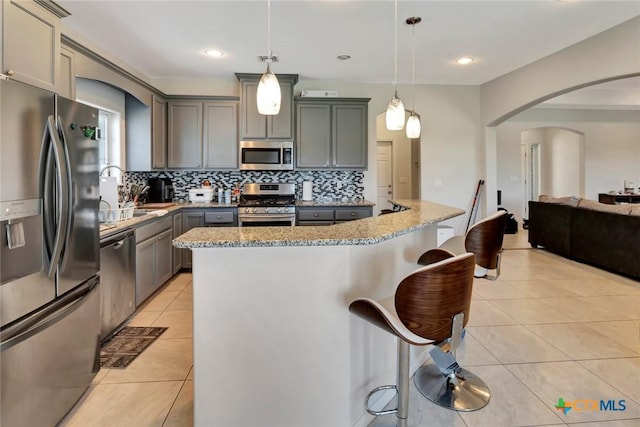 kitchen featuring light tile patterned flooring, arched walkways, gray cabinetry, stainless steel appliances, and a kitchen breakfast bar