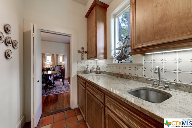 kitchen featuring backsplash, light stone countertops, sink, and dark tile patterned floors