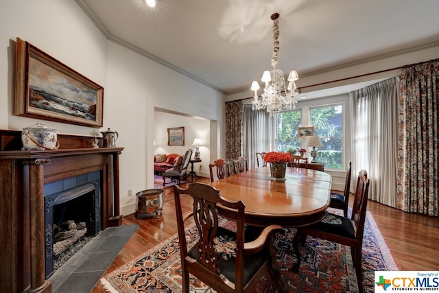 dining space featuring crown molding, a fireplace, wood-type flooring, and a notable chandelier