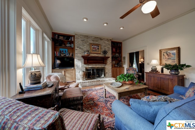 living room featuring built in shelves, ceiling fan, crown molding, and a brick fireplace