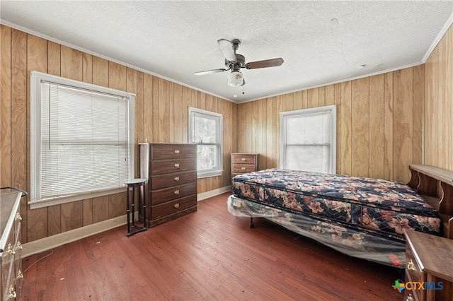 bedroom featuring dark wood-type flooring, wood walls, a textured ceiling, ornamental molding, and ceiling fan