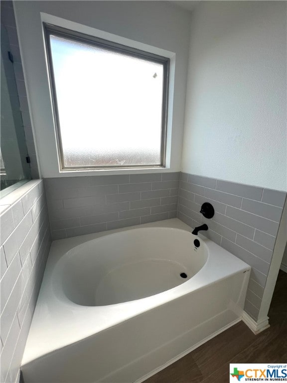 bathroom featuring a bath, wood-type flooring, plenty of natural light, and tile walls