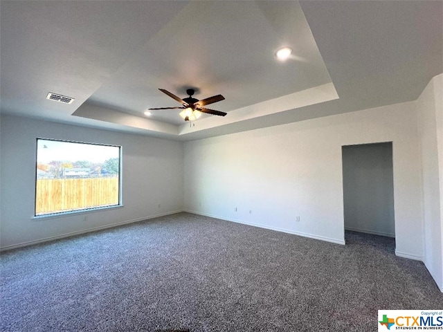 spare room with dark colored carpet, a tray ceiling, and ceiling fan