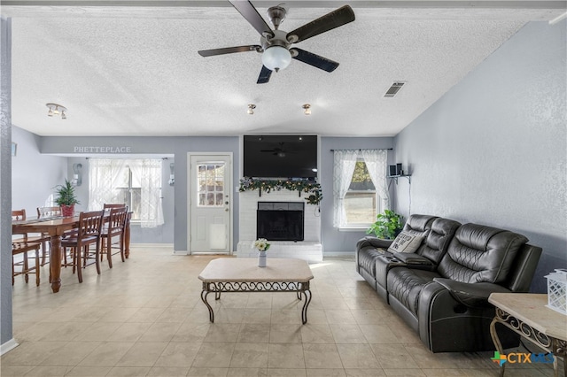 living room with a fireplace, light tile patterned floors, a textured ceiling, and ceiling fan