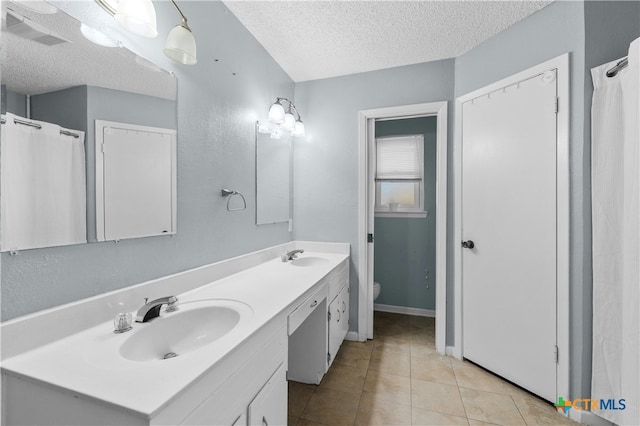 bathroom featuring tile patterned flooring, vanity, a textured ceiling, and toilet