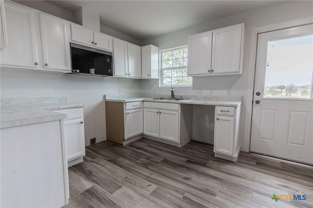 1123 Ainsworth St, Gonzales, TX 78629 - kitchen featuring stainless steel microwave, white cabinets, wood finished floors, and light countertops