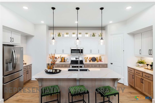 kitchen featuring stainless steel appliances, a breakfast bar area, hanging light fixtures, and light wood finished floors