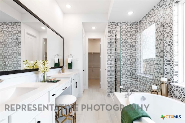 full bathroom with a spacious closet, a tub to relax in, double vanity, recessed lighting, and a sink