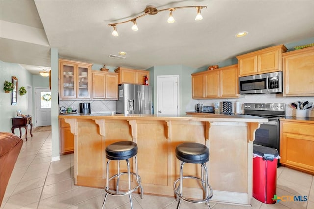 kitchen featuring a breakfast bar area, visible vents, light brown cabinetry, stainless steel appliances, and backsplash