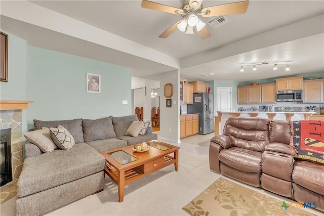 living room featuring a stone fireplace, a ceiling fan, visible vents, and baseboards