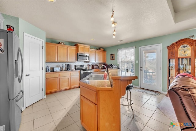 kitchen featuring backsplash, light tile patterned floors, appliances with stainless steel finishes, a kitchen breakfast bar, and a sink