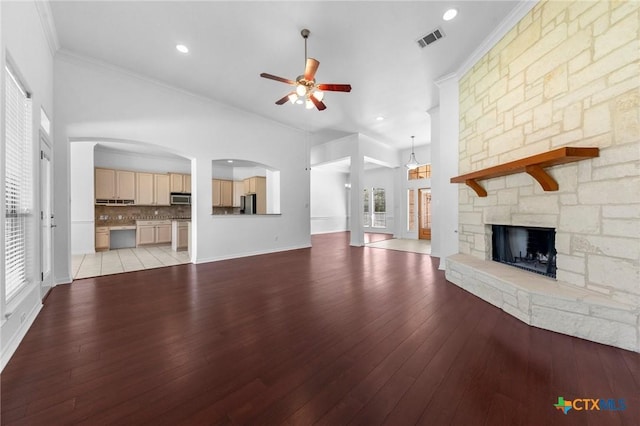 unfurnished living room with light wood finished floors, visible vents, ornamental molding, a ceiling fan, and a stone fireplace