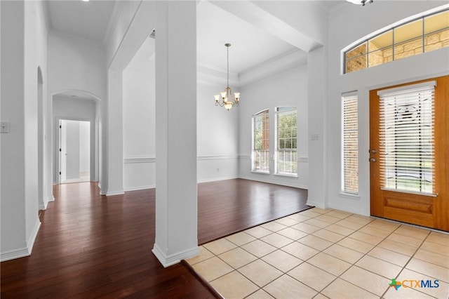 entryway featuring arched walkways, a notable chandelier, a towering ceiling, ornamental molding, and light wood finished floors