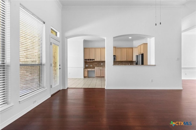 unfurnished living room featuring arched walkways, crown molding, light wood-style flooring, and baseboards