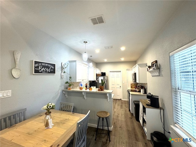 kitchen with stainless steel appliances, kitchen peninsula, a breakfast bar, white cabinetry, and decorative light fixtures