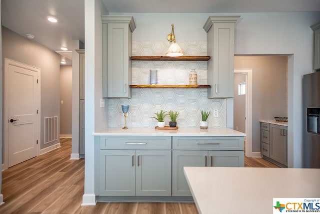 kitchen with stainless steel refrigerator with ice dispenser, tasteful backsplash, decorative columns, gray cabinetry, and light hardwood / wood-style flooring