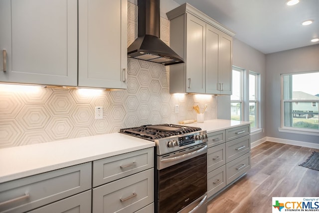 kitchen featuring wall chimney exhaust hood, backsplash, light hardwood / wood-style flooring, gray cabinets, and stainless steel gas stove