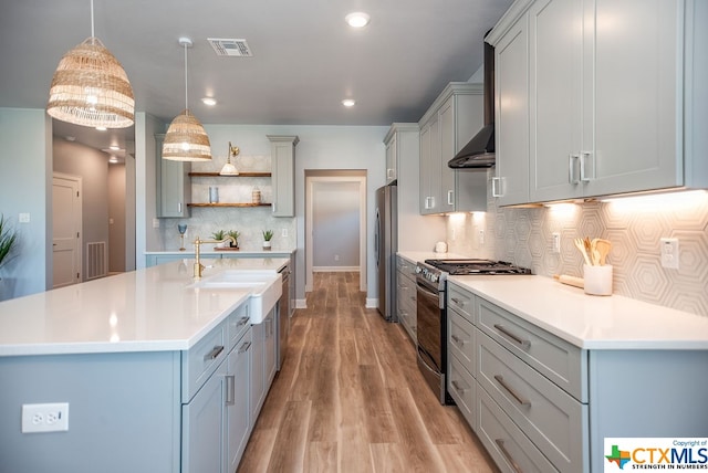 kitchen with stainless steel appliances, hanging light fixtures, tasteful backsplash, exhaust hood, and light wood-type flooring