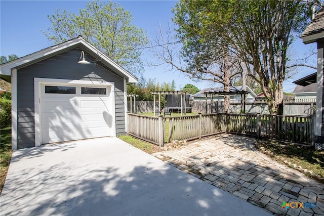 detached garage featuring fence, a trampoline, and driveway