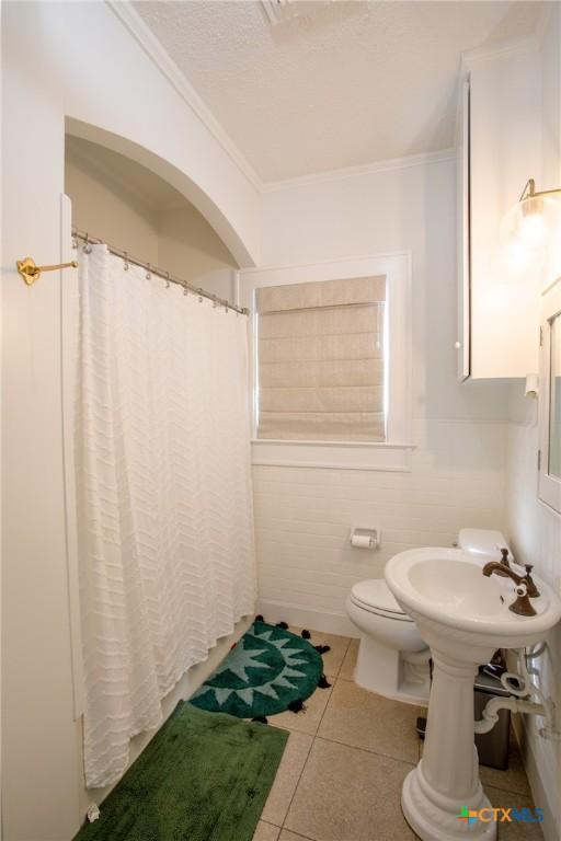 full bath with toilet, tile patterned floors, ornamental molding, and curtained shower