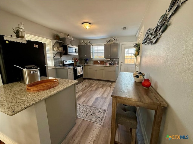 kitchen featuring sink, gray cabinets, appliances with stainless steel finishes, light stone countertops, and light wood-type flooring