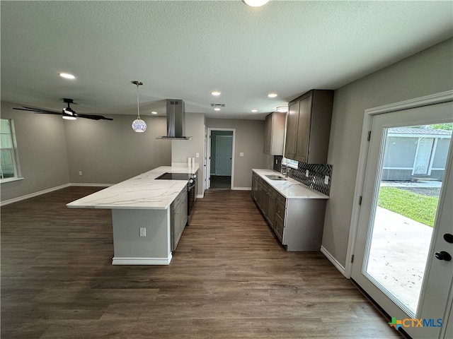 kitchen featuring sink, light stone counters, decorative light fixtures, dark wood-type flooring, and wall chimney range hood