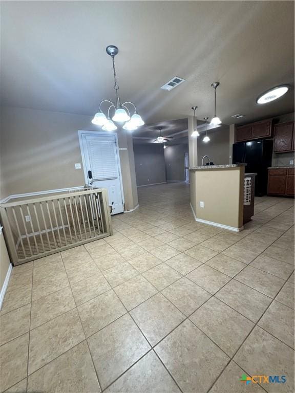 kitchen with light tile patterned floors, visible vents, light stone counters, freestanding refrigerator, and hanging light fixtures