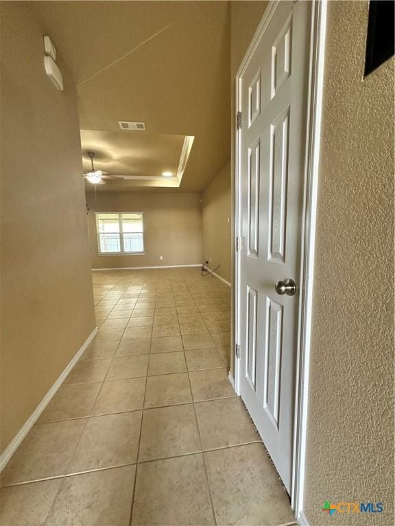 corridor featuring light tile patterned floors, a raised ceiling, visible vents, and baseboards